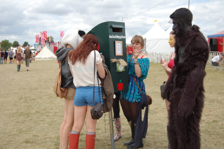 Group of festival goers stood in a field stood around a Mindapples green letterbox posting apple shaped cards with their ideas of their 5 a day for the mind.