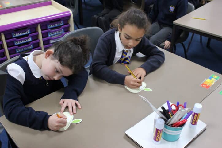 Two school children writing their applecards on a desk. Mindapples promote positive mental health from an early age.